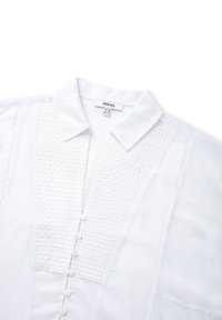 Camicia bianca con colletto. Il pannello testurizzato presenta un motivo intrecciato. Chiusura frontale con bottoni piccoli. Tessuto morbido.