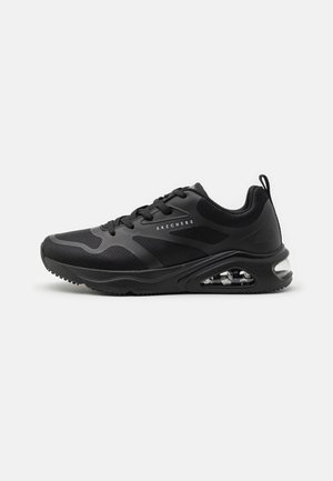 Chaussure de sport noire avec une tige en maille, semelle rembourrée et détail de poche à air transparente. Présente des motifs texturés et des lacets pour ajuster le maintien.