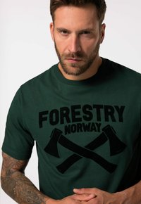 Grøn bomulds t-shirt med en iøjnefaldende sort tryk af økser og teksten "FORESTRY NORWAY", med rund halsudskæring og korte ærmer.