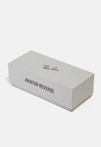 Balení Ray-Ban Aviator Reverse, obdélníková šedá kartonová krabice, obsahuje černý text, hladký povrch, minimalistický design a čisté hrany.