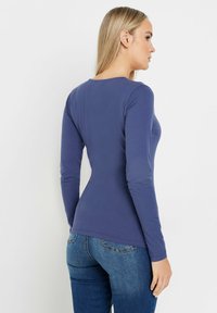 Camicia a maniche lunghe color navy con scollo rotondo e design aderente. Tessuto morbido con una consistenza liscia, abbinata a jeans in denim blu.