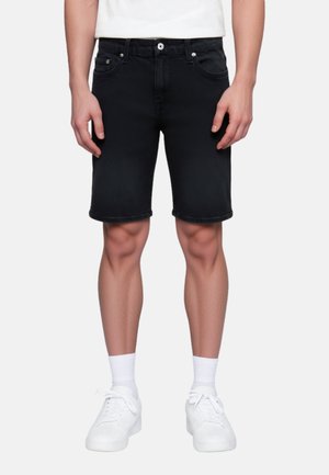 Pantalones cortos de mezclilla negra con un leve estiramiento, cinco bolsillos y un corte recto. Combinados con zapatillas blancas y calcetines. Textura suave.