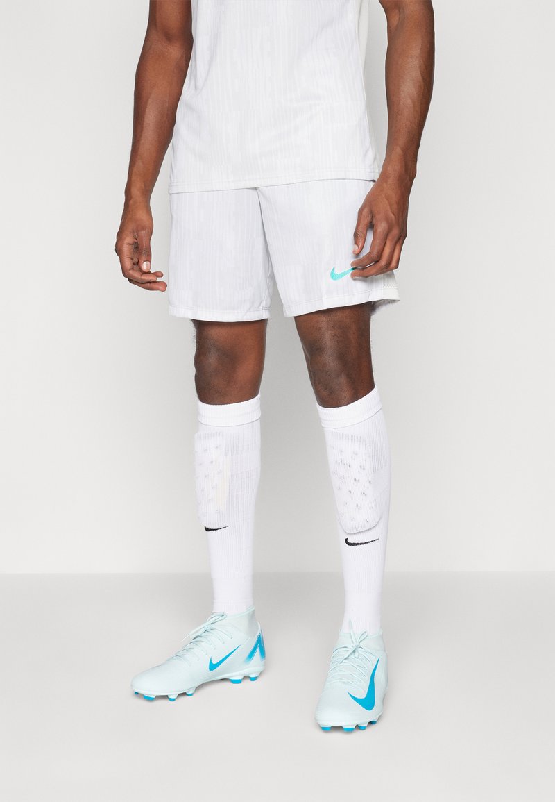 White athletic jersey and shorts, featuring light vertical patterns. Light blue soccer cleats with black accents and white socks with subtle design.