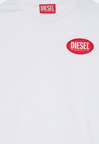 T-shirt en coton blanc avec un col rond. Présente un logo oval rouge avec le texte "DIESEL" et "POUR UNE VIE RÉUSSIE" en blanc.