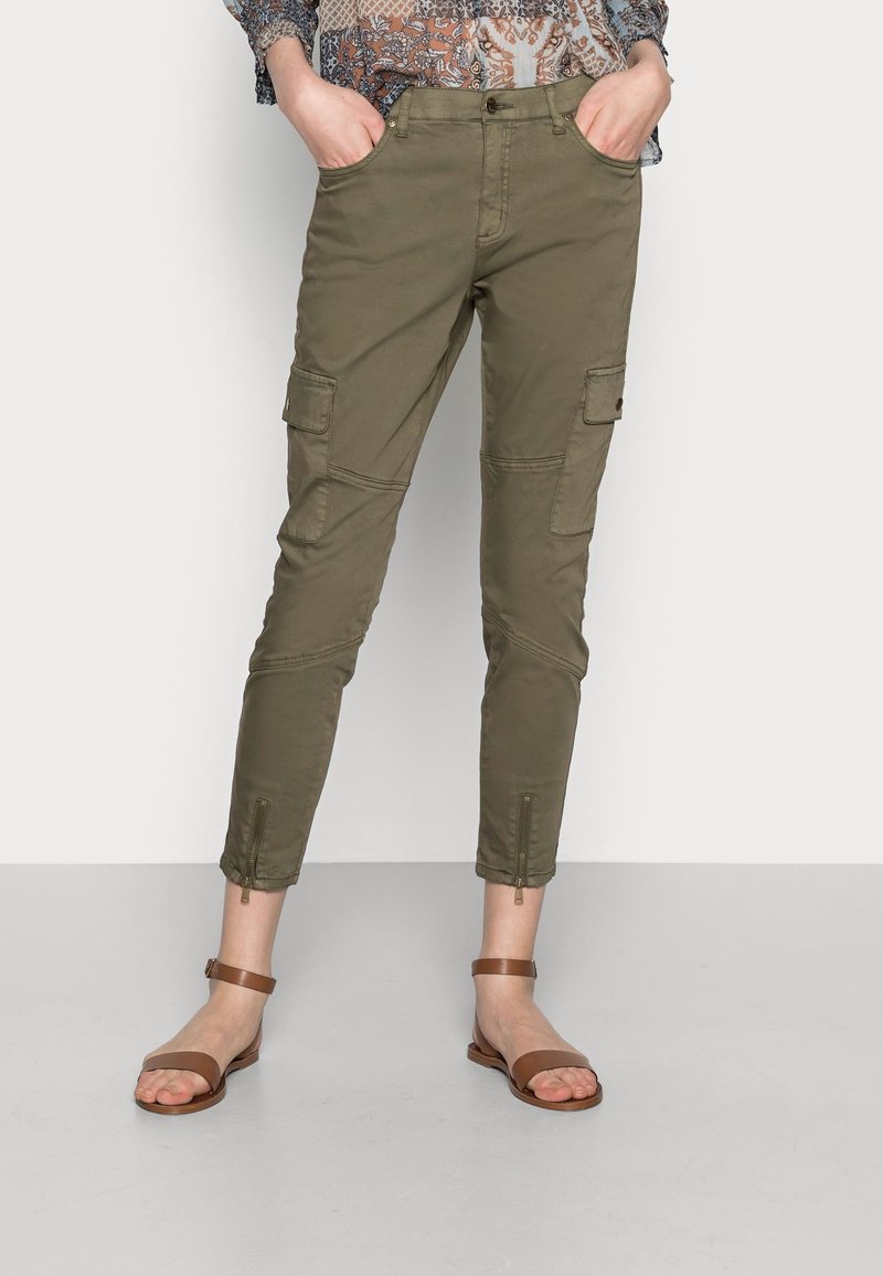 Olive green cargo pants with zipper hems, multiple pockets, and a fitted design. Paired with brown flat sandals.