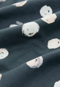 Mjuk bomullstyg i mörkblått med ett mönster av ljusbeige cirkulära former som har abstrakta ansiktsdesigner. Slät textur med lätt stretch.