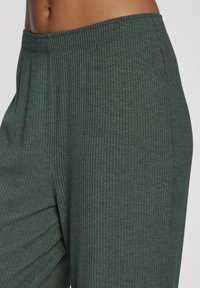 Zelene pletene hlače s širokim elastičnim pojasom. Imaju vertikalnu rebrastu teksturu i mekan, prozračan materijal. Nema vidljivih džepova.