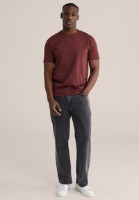 Donkerrode katoenen T-shirt met korte mouwen gecombineerd met donkergrijze spijkerbroek. Witte sneakers maken de outfit compleet. Simpel en modern ontwerp.