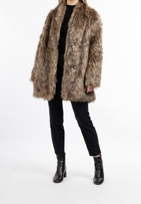 Abrigo de piel sintética marrón con acabado texturizado, mangas de longitud media y diseño de frente abierto, combinado con pantalones negros ajustados y botines hasta el tobillo.