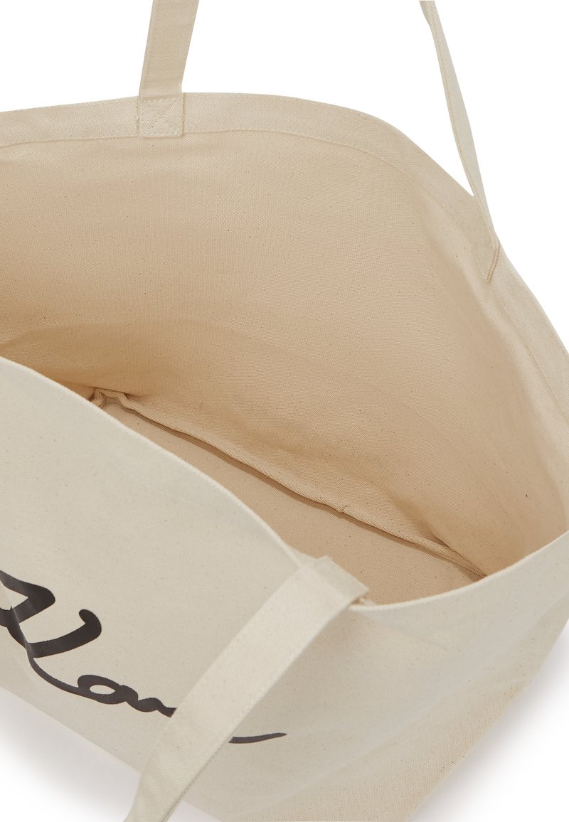 Bolso de lona en beige con diseño de texto en negro. Interior espacioso sin compartimentos adicionales. Asas de tela para llevar.