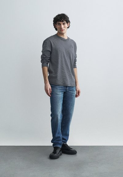 Hosszú ujjú, szürke és fekete csíkos felső világoskék farmerrel és fekete tornacipővel párosítva, laza szabással és kerek nyakkivágással.