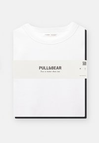 Witte t-shirt van Pull&Bear, plat gelegd met een zwart label, waarop de merknaam en een slogan staan. Eenvoudig ontwerp, standaard ronde hals.