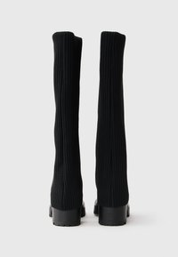 Knee-high black ribbed stretch boots with a square toe and chunky black heel, featuring a textured fabric that hugs the leg.