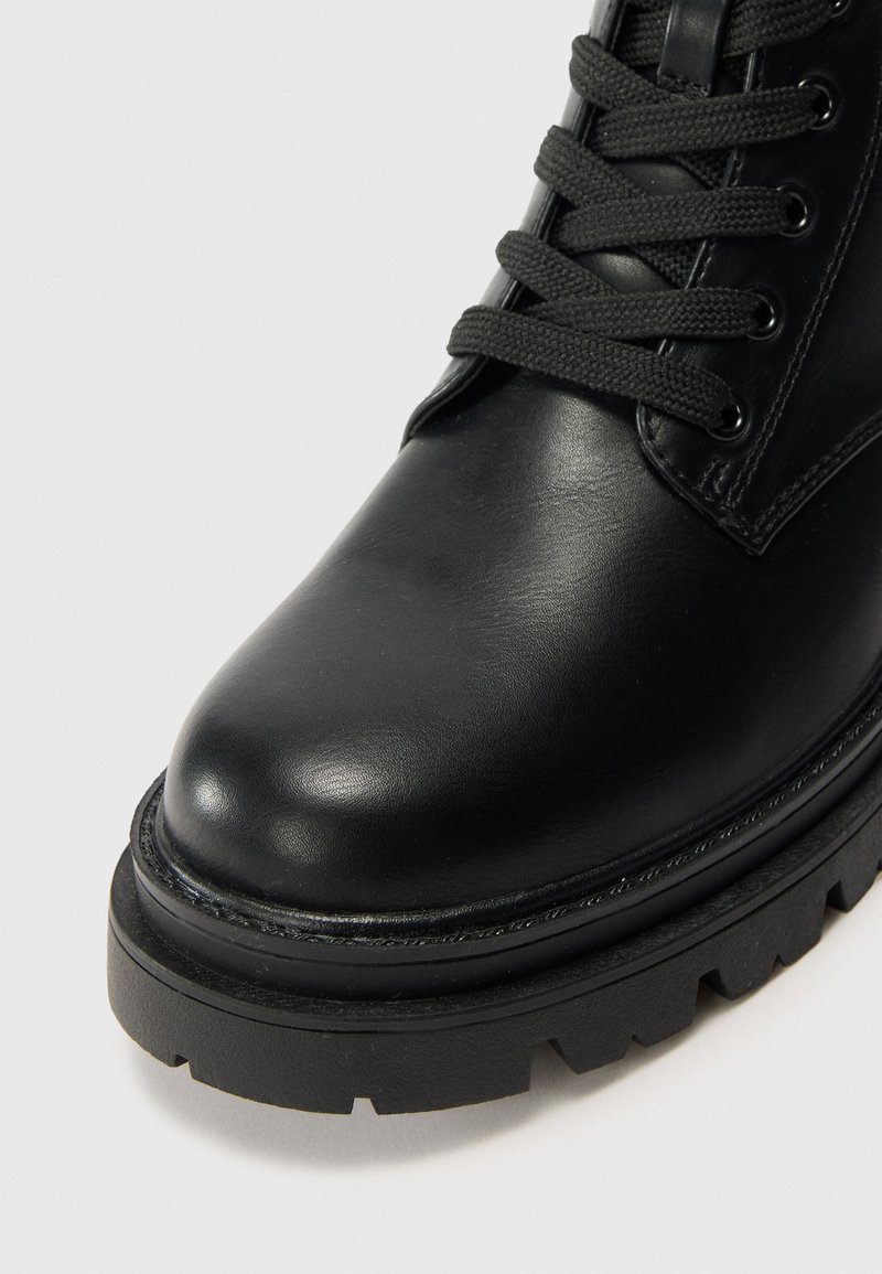 Stivale alla caviglia in pelle nera con punta arrotondata, superficie texturizzata, occhielli rinforzati, lacci neri e una suola spessa e robusta.