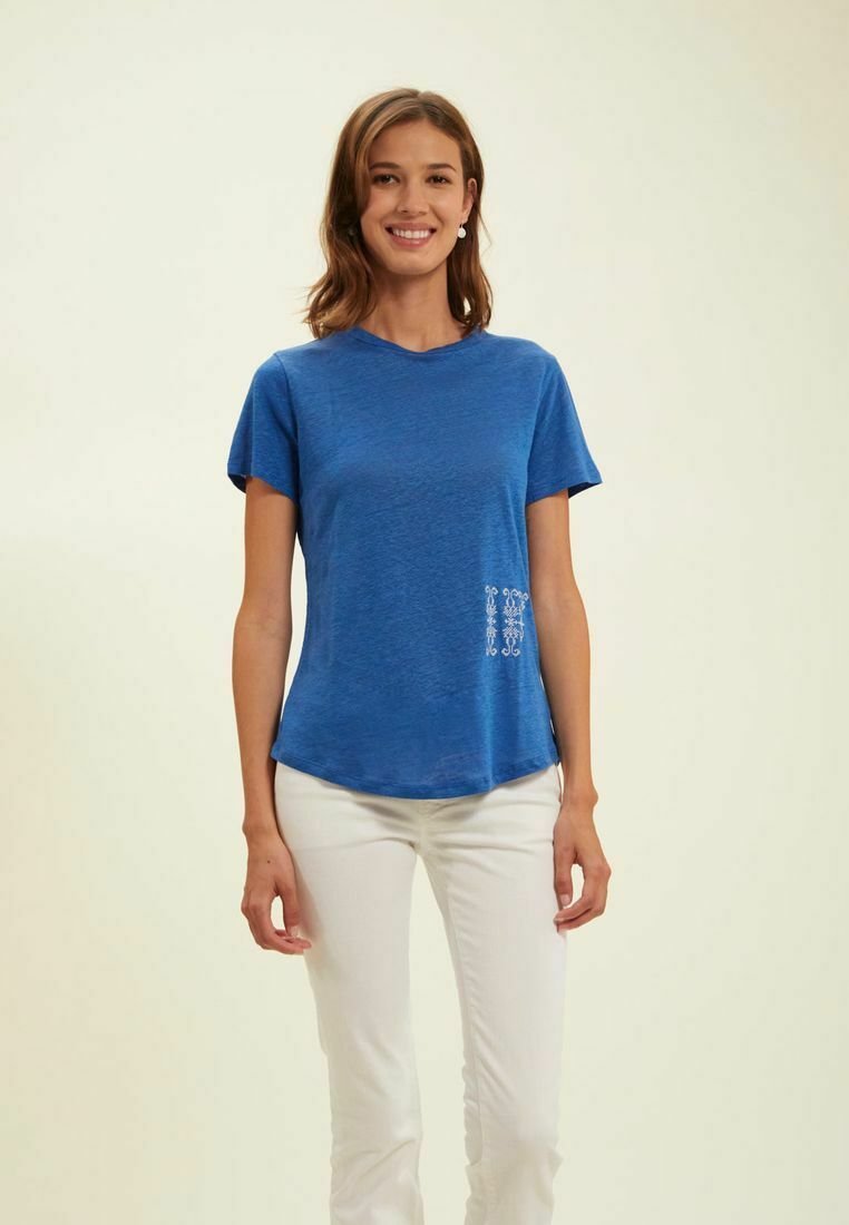 T-shirt bleu à manches courtes en tissu doux, avec un ourlet incurvé et un détail brodé blanc sur le côté inférieur gauche.