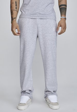 Gray sweatpants in a soft, textured fabric; tapered design with a white logo near the waistband, paired with white sneakers.
