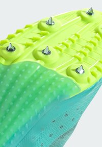 Green and yellow athletic shoe sole featuring metal spikes, textured grip pattern, and a smooth, semi-transparent section.