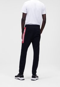 Svarta joggers med sidotape i röd logo, elastisk midja och mjukt tyg. Bärs tillsammans med en vit t-shirt och svarta träningsskor.