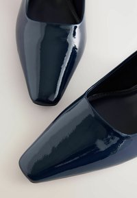 Navy sininen lakatun nahkakengät, joissa on terävä kärki, sileä kiiltävä pinta ja tyylikäs, minimalistinen muotoilu.
