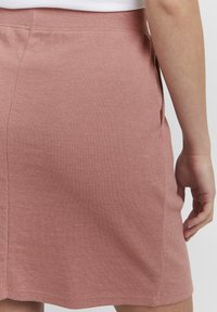 Rosa ribbestrikket skjørt med en tilpasset livlinje og sidelommer, med rett kant og en myk tekstur.