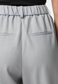 Gai pelēki bikses ar savāktu jostasvietu, ar divām aizmugures kabatām ar plakanu atveri. Gluda tekstūra un strukturēts dizains.
