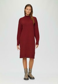 Bordeauxfarbendes Strickkleid mit langen Ärmeln, hohem Kragen und gerippten Bündchen und Saum, kombiniert mit beigen Knöchelstiefeln. Glatte Textur und lockere Passform.