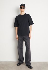 Maglietta nera oversize, jeans grigi scuri a gamba larga, occhiali da sole neri e berretto abbinato. Tessuto morbido con una silhouette casual e rilassata.