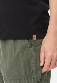 Sort bomulds t-shirt med rundet søm og et lille brunt logo mærke. Olivengrønne fløjl-bukser med ribbet tekstur og sidesøm.