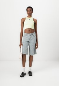 Ljust grön croppad ärmlös topp, urblekta blå denimbermudashorts, vita strumpor, svarta skor och en liten ljusrosa handväska.