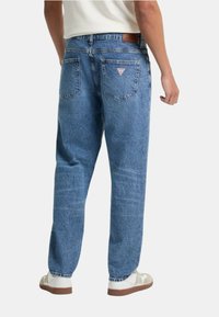 Jeans in denim azzurro chiaro con vestibilità rilassata, dotati di tasche posteriori con toppe a forma triangolare e un'etichetta in pelle marrone sulla vita.