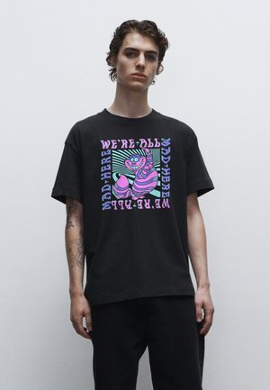T-shirt en coton noir à manches courtes avec un imprimé rectangulaire coloré représentant un chat rose souriant et du texte en violet et vert.