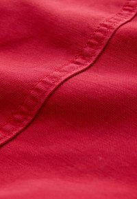 Vue en gros plan d'un tissu rouge texturé avec une couture visible cousue en diagonale à travers la surface.