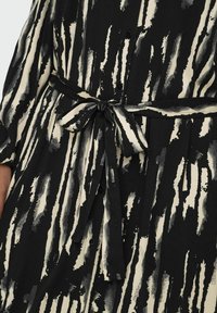 Robe noire et crème avec un motif de coups de pinceau verticaux, dotée d'une taille nouée et de détails en boutons, fabriquée dans un tissu doux.