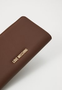 Portafoglio in pelle marrone con il logo dorato "LOVE MOSCHINO" centrato sul davanti, esposto su uno sfondo bianco semplice.