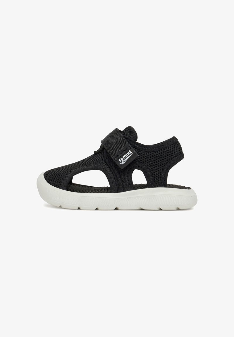 Sandale en mesh noir respirant avec semelle blanche flexible et bride Velcro ajustable sur fond blanc.