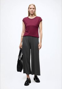 Maroon short-sleeve top paired with loose, dark gray wide-leg pants. Black shoes and a black tote bag complete the outfit. Simple and modern design.