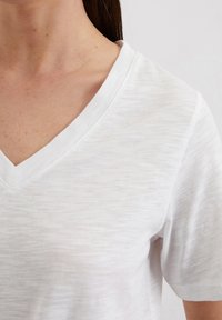 Valge V-kaelusega T-särk, mis on valmistatud kergest, kergelt tekstuuriga kangast. Omab lühikesi varrukaid ja lõtvamat lõiget, millel on peen värvi varieerumine.