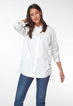 Witte katoenen overhemd met knoopsluiting en lange mouwen, zijachtige trekkoorddetails en een relaxte pasvorm, gecombineerd met blauwe denim jeans.
