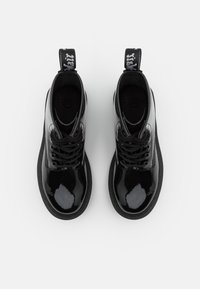 Botas de cordones de cuero negro brillante con suelas gruesas y tiradores con marca, vistas desde arriba sobre un fondo blanco.