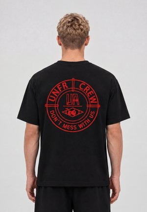 Bagfra visning af en person iført en sort t-shirt med et rødt rundt logo med teksten "UNFR CREW" og "DON'T MESS WITH US" på bagsiden.
