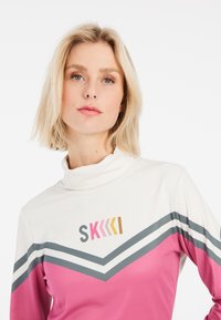 Dugi rukavi turtleneck majica u bijeloj, ružičastoj i sivoj boji s chevron uzorkom i logotipom. Glatki materijal s preklopom ovratnika i prilagođenim dizajnom.