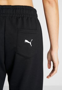 Zwarte joggingbroek met een zachte textuur, voorzien van een achterzak en een wit Puma-logo. Elastische tailleband voor comfort.