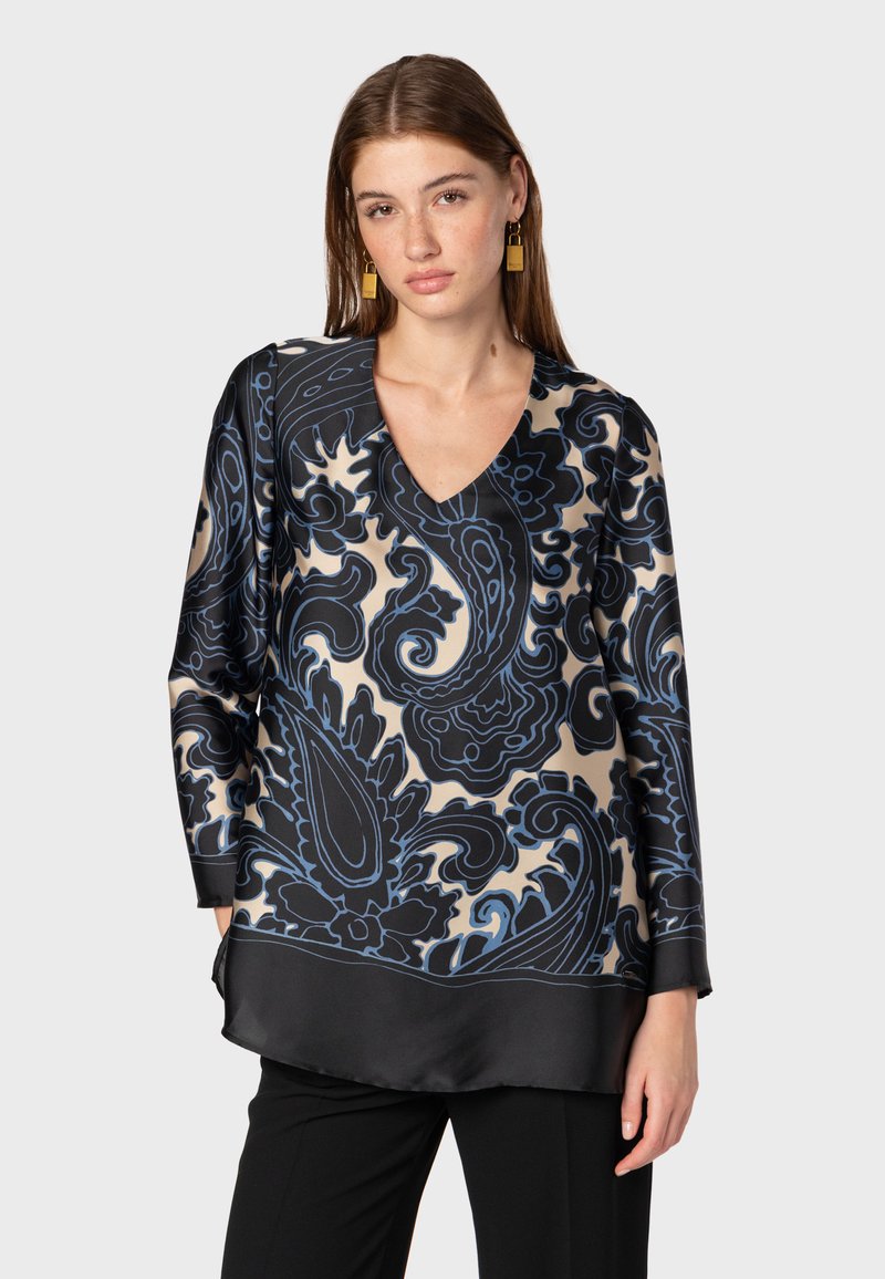 Blusa a maniche lunghe in satin beige con un motivo paisley nero e blu, caratterizzata da un collo a V e un orlo nero. Texture liscia.