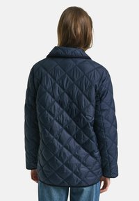 Marineblaue gesteppte Jacke mit Diamantmuster, ausgestattet mit einem Kragen und langen Ärmeln. Weiche Textur und lockere Passform, geeignet zum Schichten.