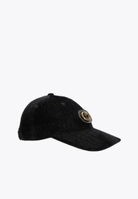 Casquette noire avec une surface texturée et un motif matelassé. L'avant présente un badge métallique circulaire avec un design complexe.