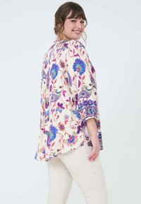 Vloeiende crème blouse met levendige bloemen- en paisleyprint. Heeft brede mouwen en een afgeronde zoom. Accenten in felroze en blauw.