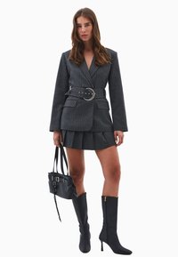 Grå jakkesæt med striber, skræddersyet blazer, bæltedesign, matchende miniskirt og knæhøje sorte stiletto støvler. Inkluderer sort håndtaske.