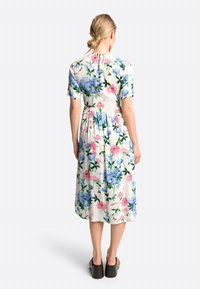 Abito midi floreale in tessuto leggero con maniche corte. Presenta fiori blu e rosa su uno sfondo crema. Vita elasticizzata e scollo rotondo.