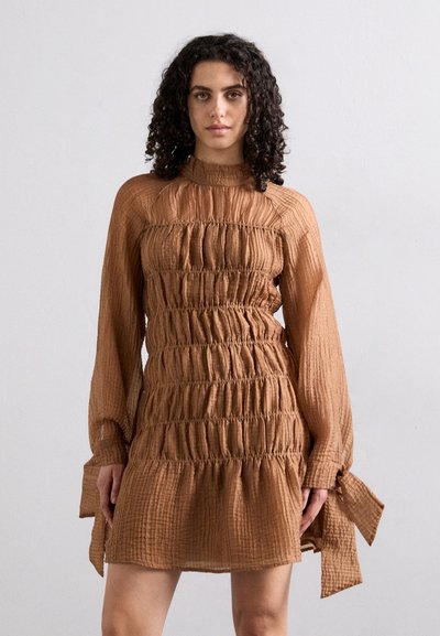 Robe marron texturée avec des manches longues, des détails froncés, un col haut et un ourlet à volants. Stylée avec des accents noués au niveau des poignets.