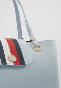Jasnoniebieska skórzana torebka z klapą w czerwono-biało-granatowe paski, złotym logo Tommy Hilfiger i okuciem oraz podwójnymi ramiączkami.